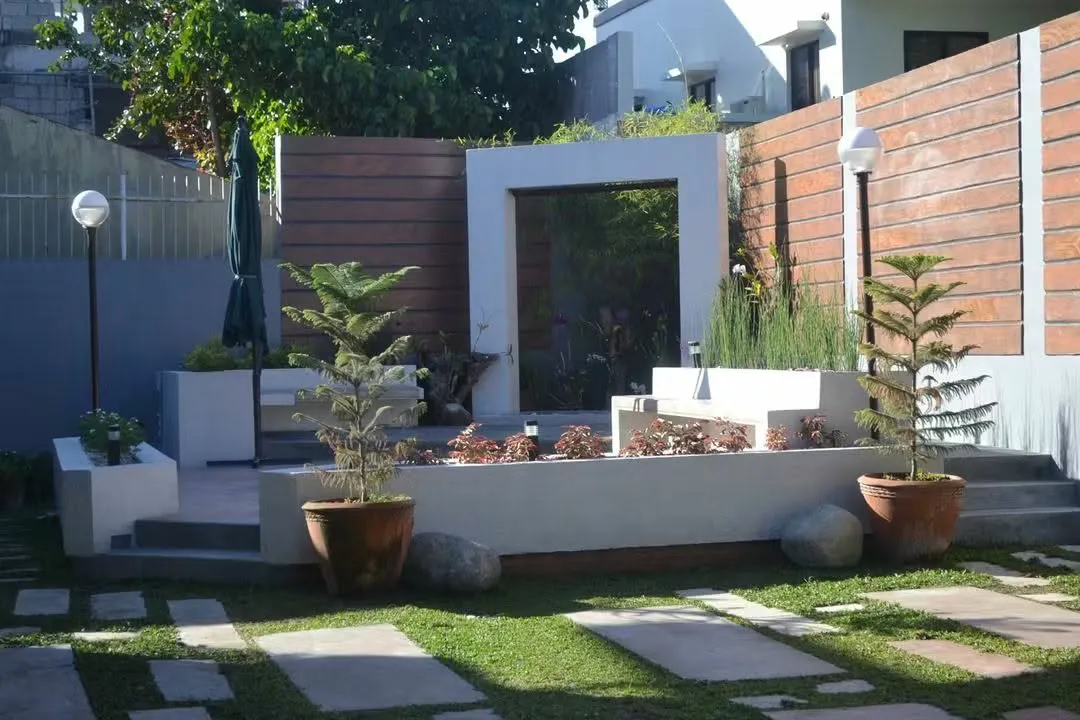 The garden in daylight: a lawn with stepping stones, raised planters and potted pines, 2015