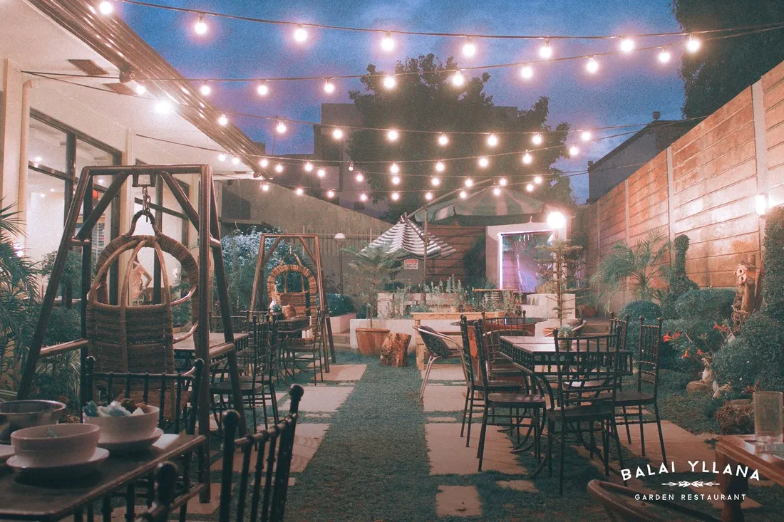 Garden tables under string lights at dusk, with a hanging swing chair, 2017