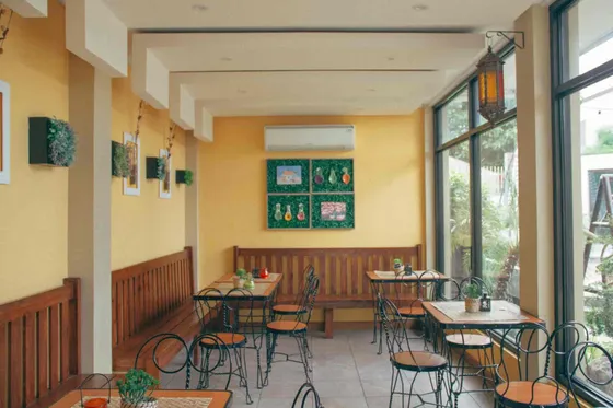 The sunroom with yellow walls, wooden benches and iron chairs, 2017